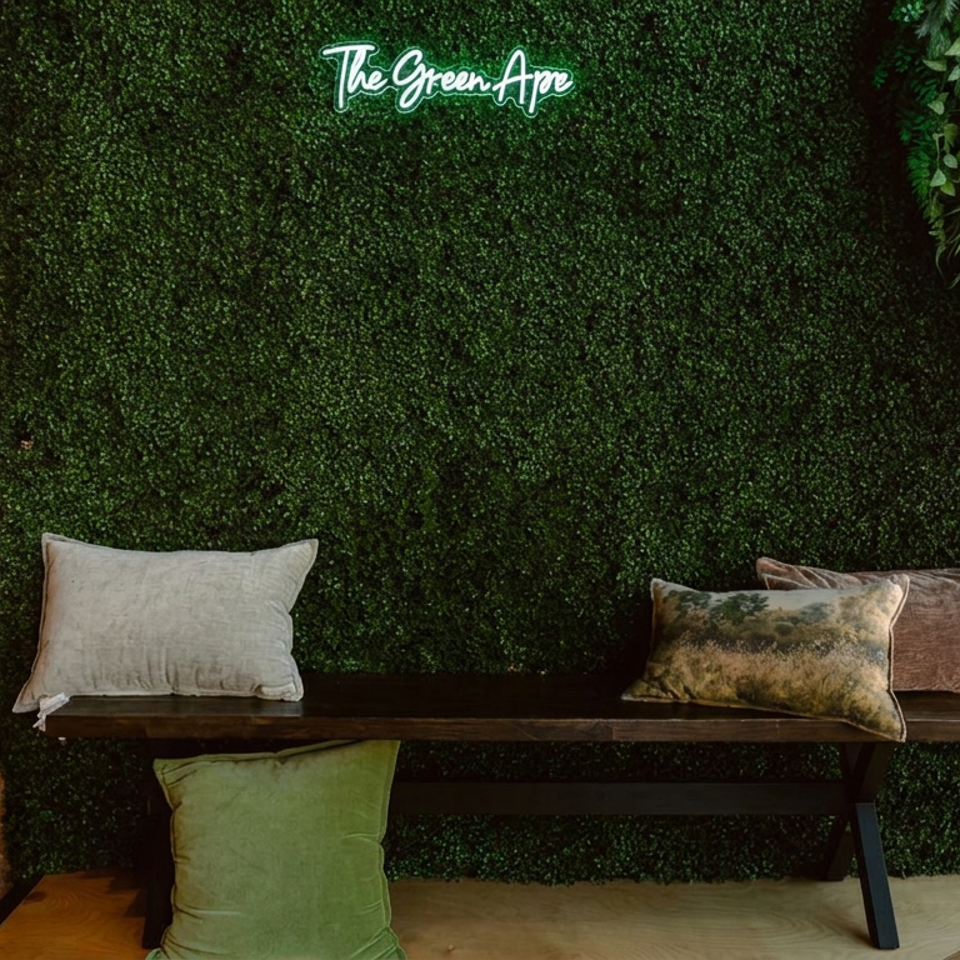 Cozy restaurant seating area with a wooden bench, cushions, brick wall, greenery backdrop, and The Green Ape sign.